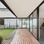 Casa moderna con ampie vetrate scorrevoli, pavimento in legno e giardino, dal design minimalista e dalle linee essenziali.