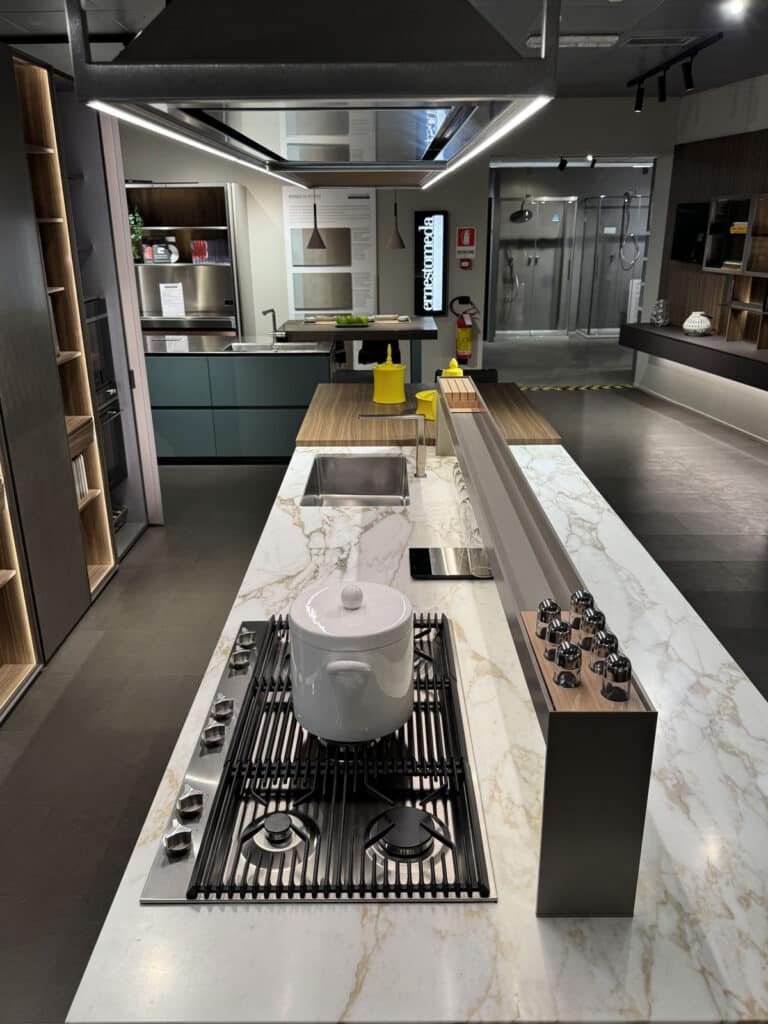 Isola cucina con piano cottura a gas e top in marmo bianco in un allestimento showroom