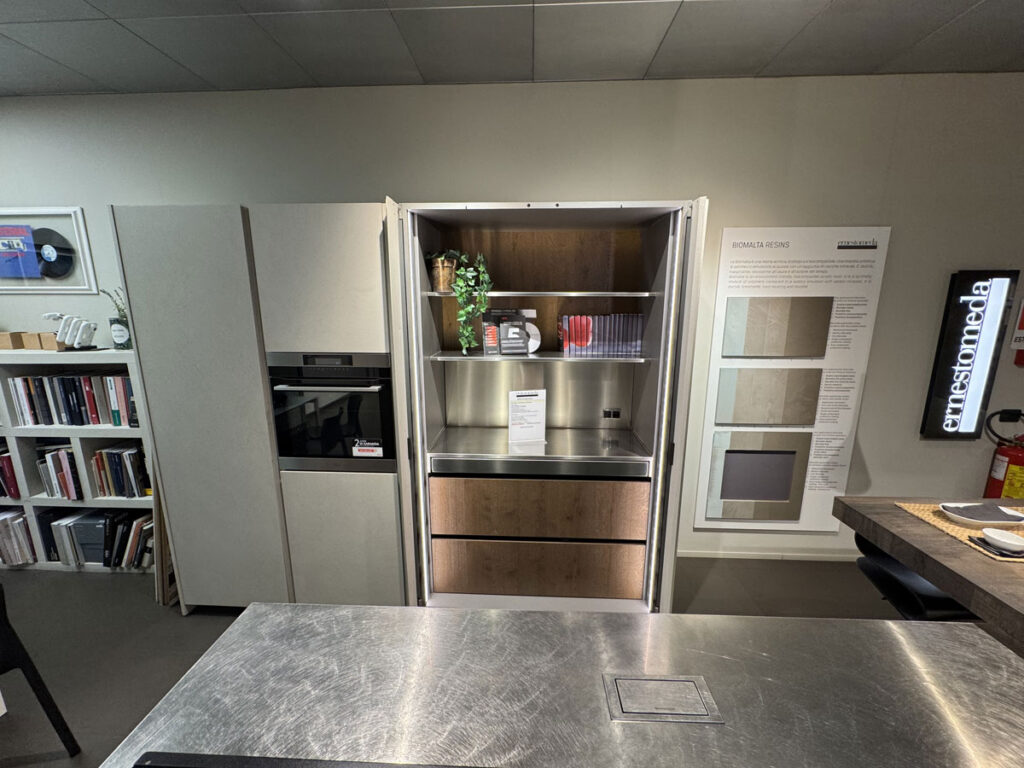 Cucina moderna Arredo 3 con elettrodomestici da incasso, libreria e campionari delle finiture Tre P a parete.