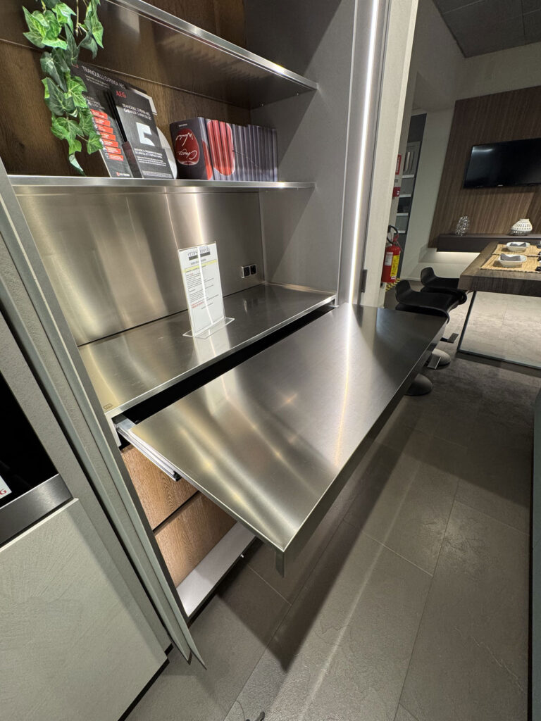 Cucina moderna Arredo 3 con piano estraibile in acciaio, mensole e zona pranzo sullo sfondo.
