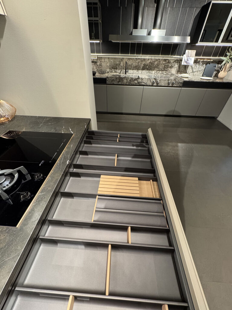 Cucina moderna Arredo 3 con mobili scuri, cassetto organizzato e zona lavello; sullo sfondo, la cucina Obliqua.