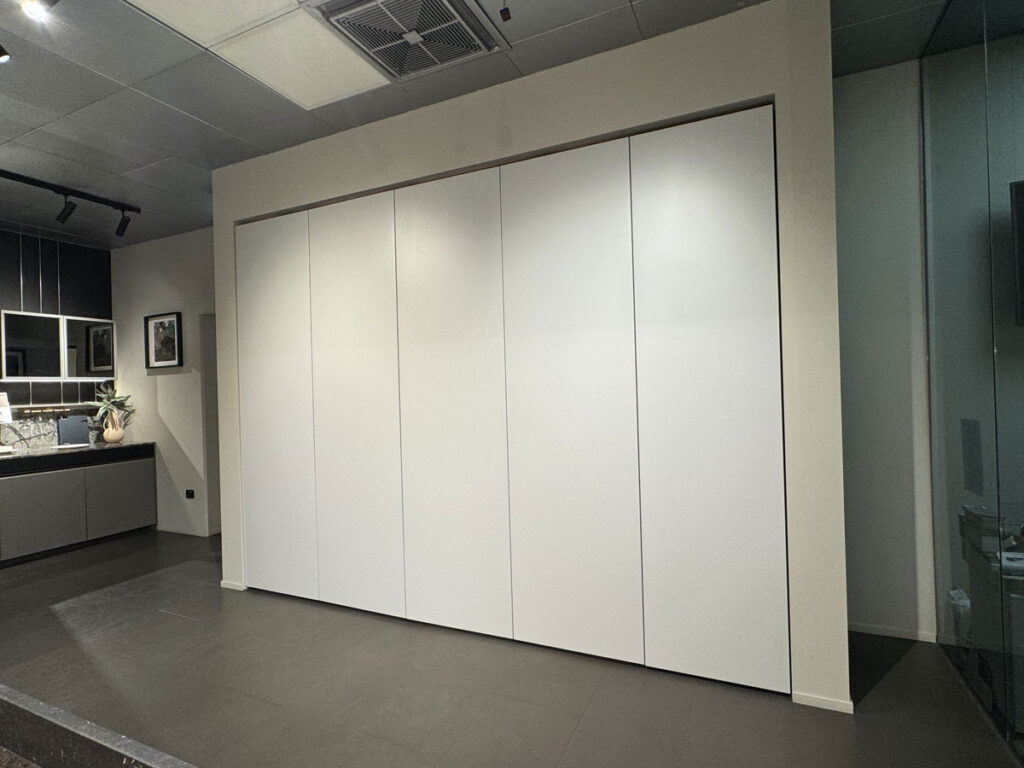 Cucina Ernestomeda con armadi bianchi a tutta altezza e pavimento scuro, illuminazione moderna e mensole a vista.