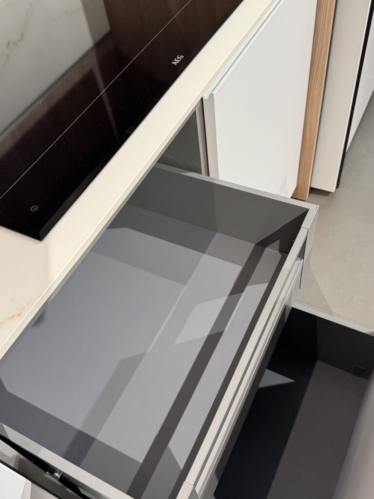 Moderna cucina Ernestomeda con due cassetti a vista dal design minimalista sotto il piano cottura in vetro nero.
