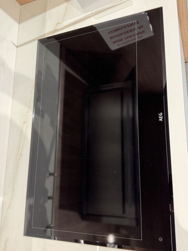 Piano cottura a induzione AEG nero su piano di lavoro in marmo bianco Ernestomeda, dalla superficie lucida e moderna.