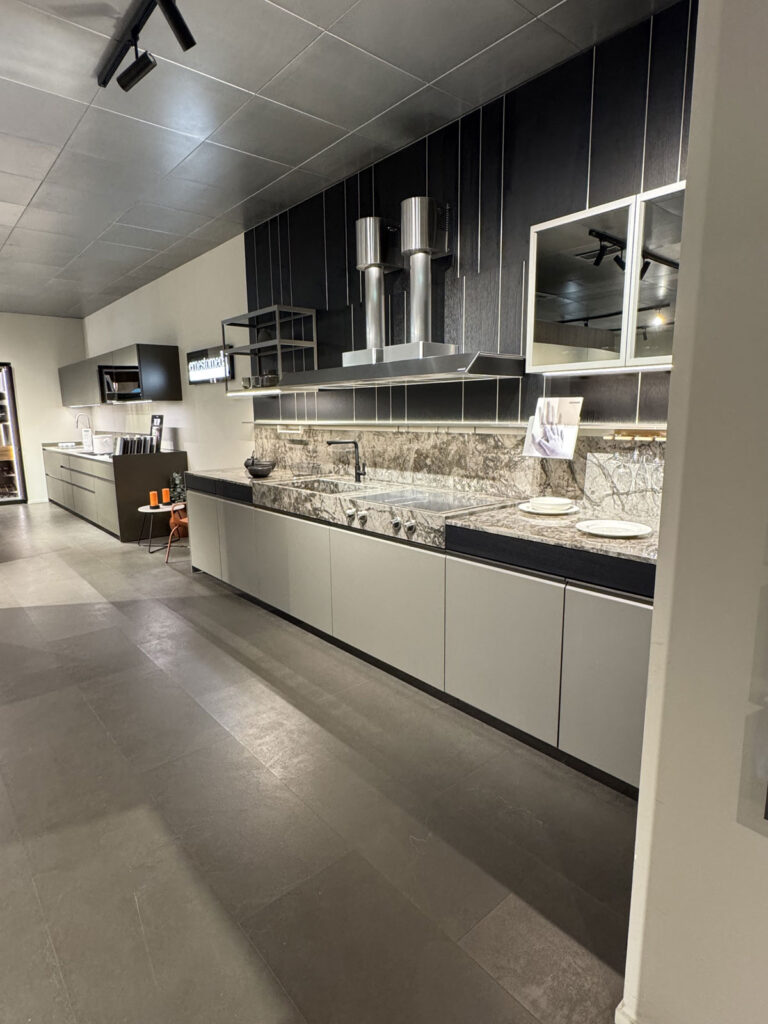 Cucina moderna con mobili grigi Ernestomeda, piano di lavoro e paraschizzi effetto marmo, cappa in acciaio inossidabile e luci integrate.