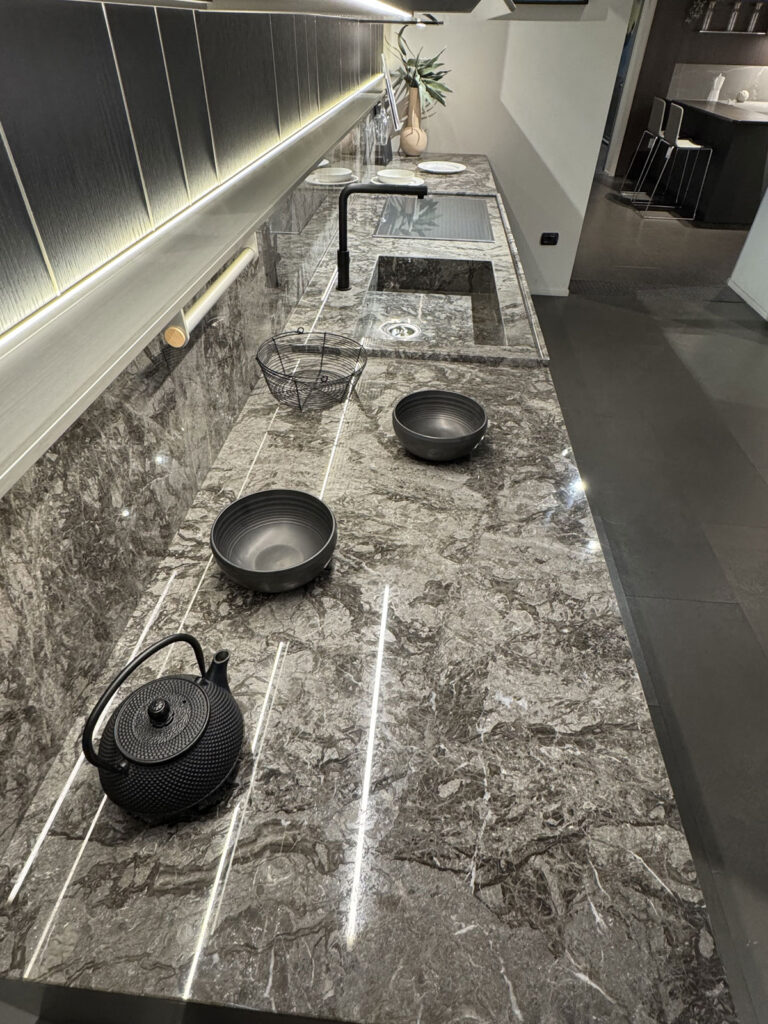 Moderna cucina Ernestomeda con piano in marmo, due pentole nere, una teiera nera e un cestino in filo metallico.