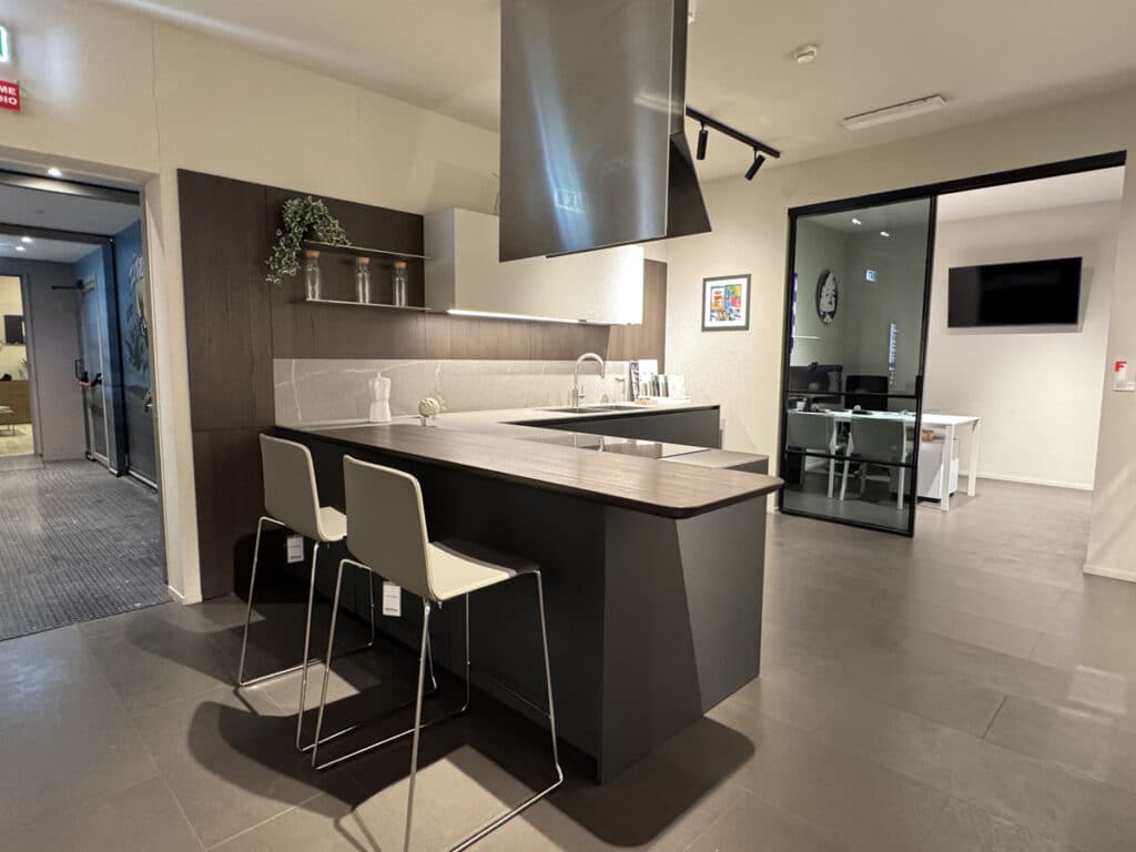 Isola cucina con sgabelli e cappa a soffitto in un allestimento Ernestomeda in showroom