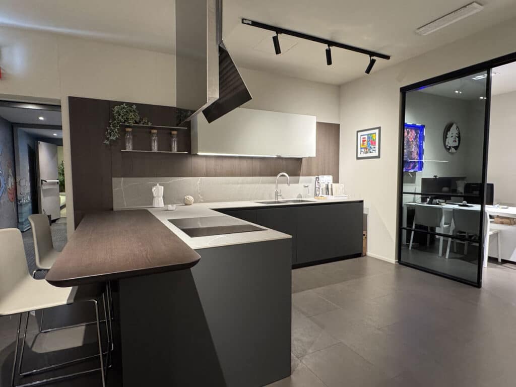 Cucina Ernestomeda con penisola, top scuro e cappa a soffitto in ambiente showroom