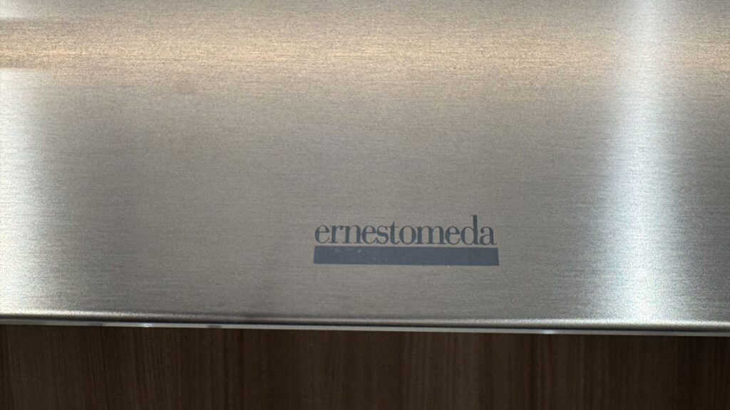 Dettaglio del logo Ernestomeda inciso su metallo satinato, con elegante sfondo in legno per una cucina moderna.