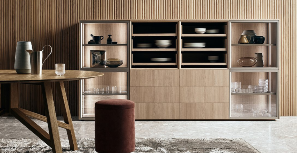Sala da pranzo moderna con tavolo rotondo in legno, mobile a giorno, pouf rosso e tappeto su pavimento in marmo.