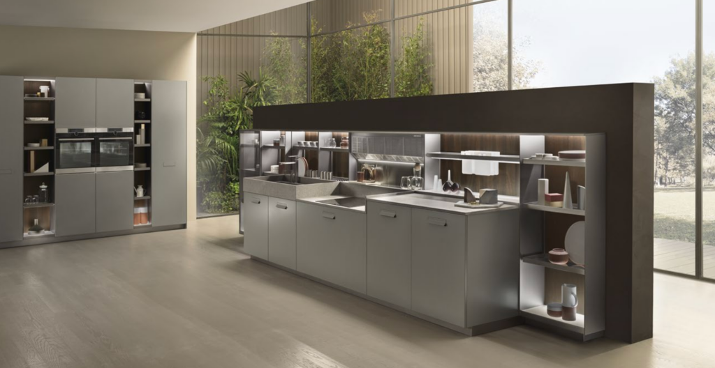 Cucina moderna con mobili grigi, elettrodomestici da incasso, mensole a vista e ampie finestre che si affacciano sul verde esterno.