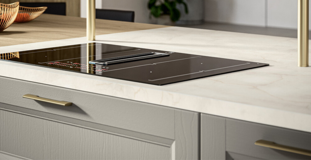 Cucina moderna con piano a induzione nero e maniglie dorate sui cassetti grigi, tavolo in legno sullo sfondo.