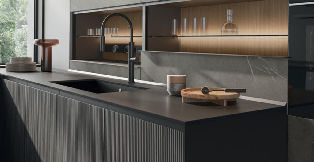 Cucina moderna con piano di lavoro nero, lavello integrato e pensili in legno su uno sfondo di marmo grigio.