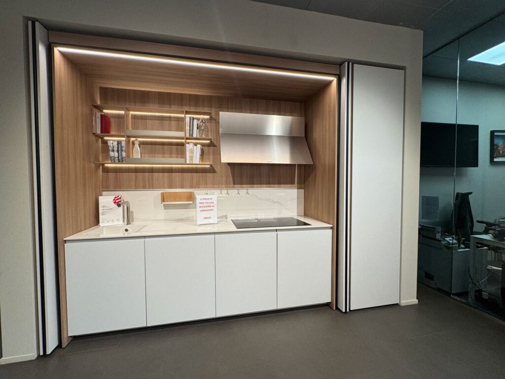 Cucina moderna con mobili bianchi, paraschizzi in legno, mensole a vista, piano cottura a induzione e cappa in metallo.