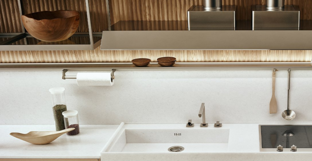 Cucina moderna con piano di lavoro bianco, lavello integrato e fornelli; stile minimalista e colori neutri.