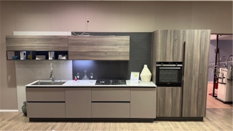 Cucina moderna con mobili in legno chiaro e grigio, piano di lavoro bianco, forno e piano cottura da incasso, parete scura sullo sfondo.