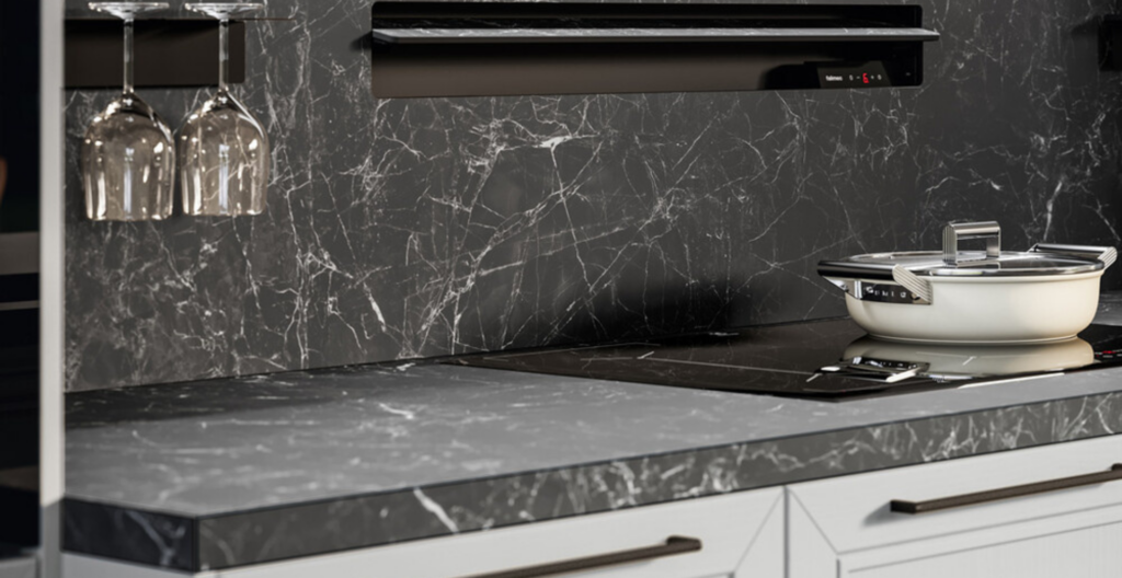 Cucina moderna con piano di lavoro e parete in marmo nero, pensili bianchi e piano cottura a induzione con pentola bianca.