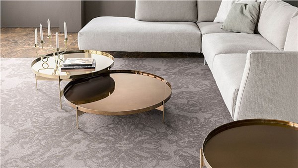 Divano chiaro ad angolo con tavolini tondi in ottone su tappeto decorato