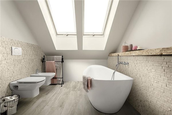 Bagno in mansarda con parete in pietra, vasca freestanding e sanitari sospesi
