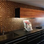 Cucina scura con schienale rivestito in mosaico dorato e lavello in acciaio