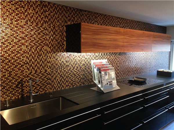 Cucina scura con schienale rivestito in mosaico dorato e lavello in acciaio