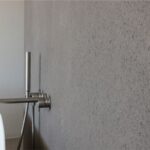 Parete in resina effetto cemento con miscelatore a colonna accanto a una vasca