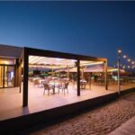 Pergotenda illuminata al tramonto sopra un'area ristorante affacciata sul mare