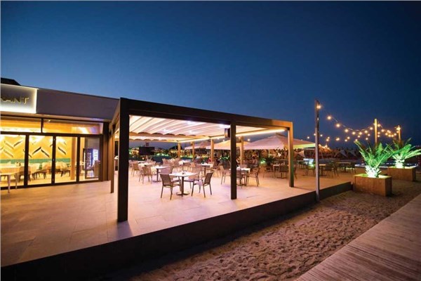 Pergotenda illuminata al tramonto sopra un'area ristorante affacciata sul mare