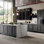 Cucina con isola, colonne scure e ampia vetrata affacciata sul verde