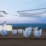 Arredi da esterno bianchi con ombrelloni a vela affacciati sul mare al tramonto