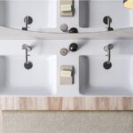 Doppio lavabo integrato in un piano con miscelatori neri e specchio tondo