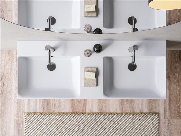 Doppio lavabo integrato in un piano con miscelatori neri e specchio tondo