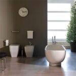 Bagno con sanitari a terra, vasca ovale e parete scura con orologio