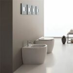 Vaso e bidet sospesi bianchi in un bagno minimale con placche di comando