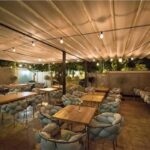 Ristorante all'aperto con copertura in legno a lamelle, tavoli e luci sospese