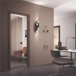 Porta a filo muro in finitura chiara aperta su uno studio con scrivania