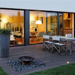 Casa con vetrate illuminate di sera affacciate su una terrazza in legno