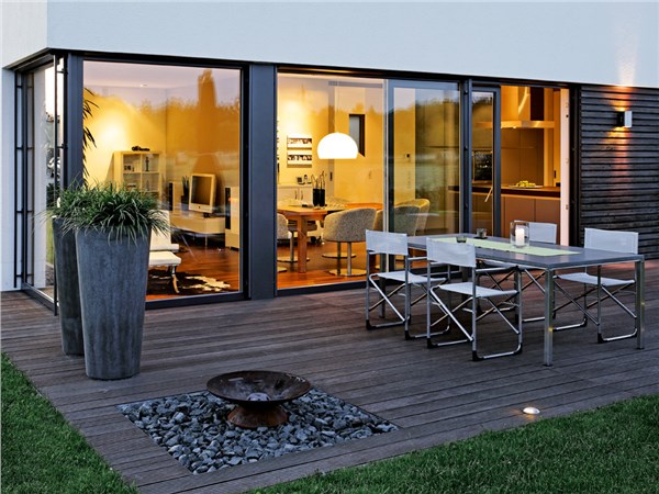 Casa con vetrate illuminate di sera affacciate su una terrazza in legno