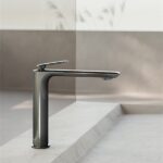 Miscelatore da lavabo alto in finitura scura su un piano in pietra chiara