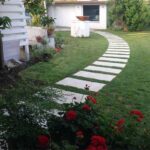 Vialetto in pietra su un prato con fiori rossi e casa sullo sfondo