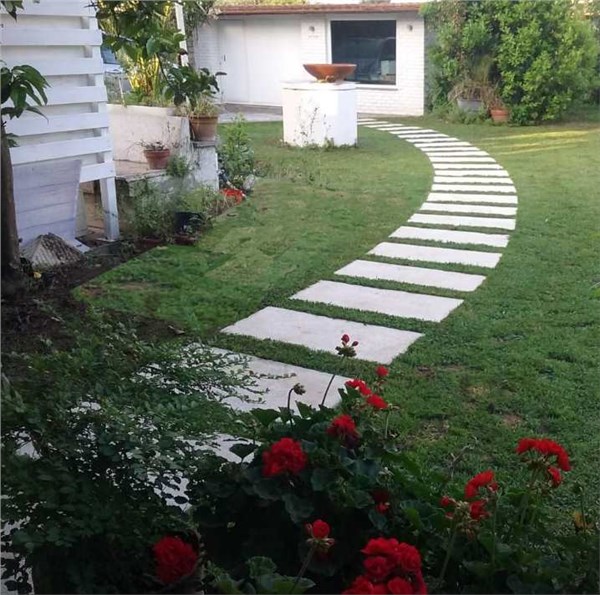 Vialetto in pietra su un prato con fiori rossi e casa sullo sfondo