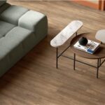 Divano verde su pavimento in gres effetto legno con tavolini tondi