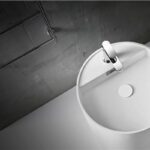 Lavabo tondo bianco su pavimento scuro con gradino e miscelatore