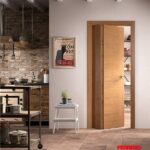 Porta in legno chiaro aperta su una cucina rustica con mattoni a vista