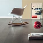 Sedia a dondolo bianca su pavimento in parquet rovere scuro con libri e lampada