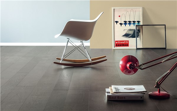 Sedia a dondolo bianca su pavimento in parquet rovere scuro con libri e lampada
