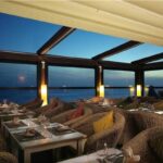Sala di un ristorante coperta da una pergotenda con vista sul mare al tramonto