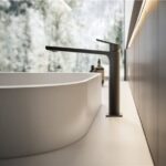 Miscelatore nero su lavabo bianco davanti a una parete effetto marmo