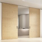 Due porte scorrevoli in legno chiaro che aprono su una stanza da bagno
