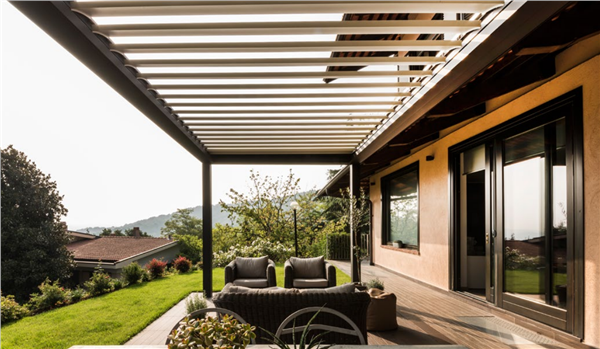 Pergola con struttura scura e lamelle orientabili sopra un'area salotto all'aperto